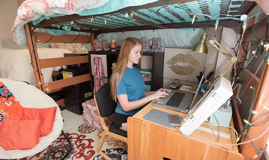 Mary Burke Hall bedroom decorated with a female student sitting under her lofted bed working on her computer