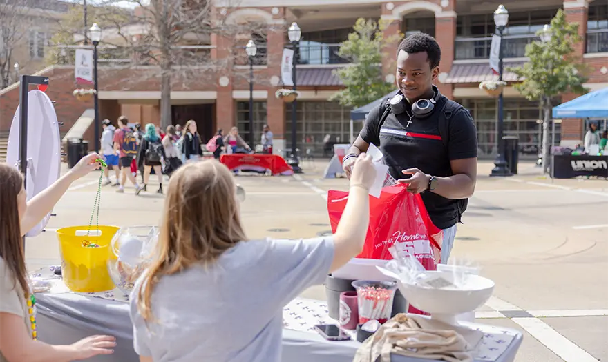 University of Alabama student attending the Off-Campus Housing Fair, standing at a table and placing informational materials into a bag